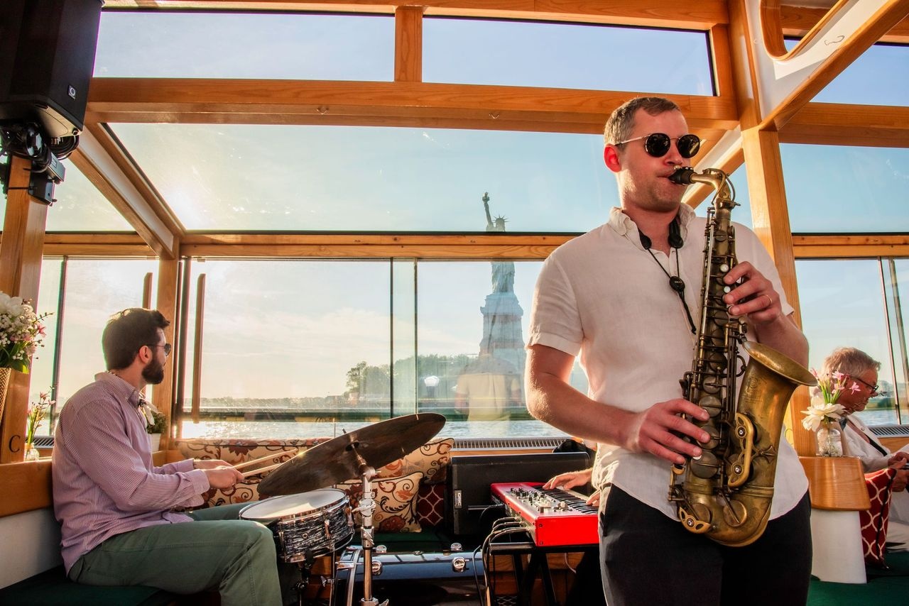 Jazz band performs on a boat with the Statue of Liberty visible in the window.