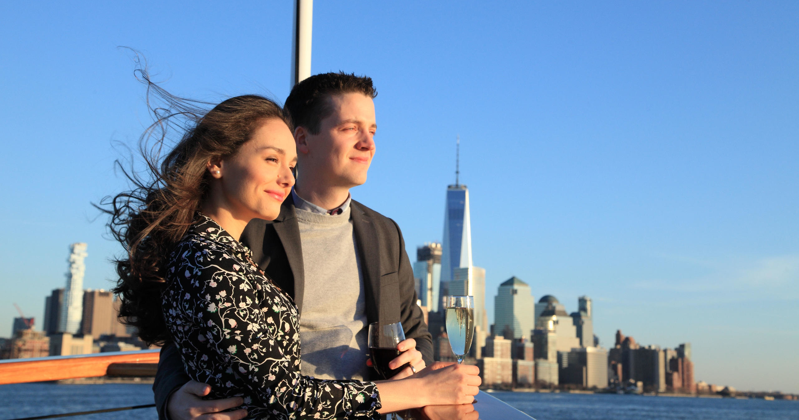 Couple embraces on boat with city skyline in background.