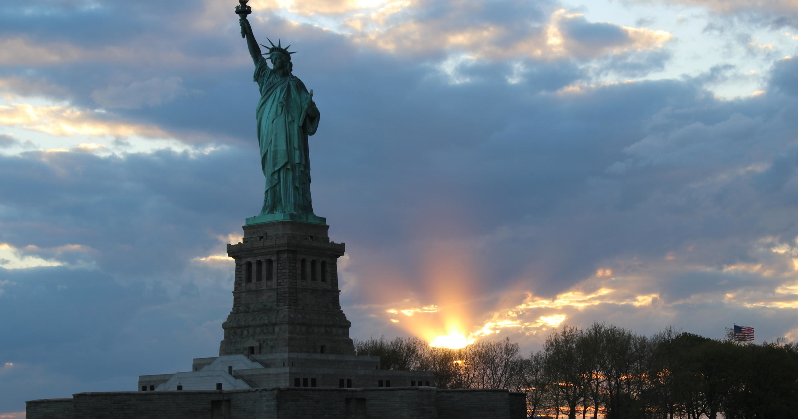 Statue of Liberty against a sunset with clouds.