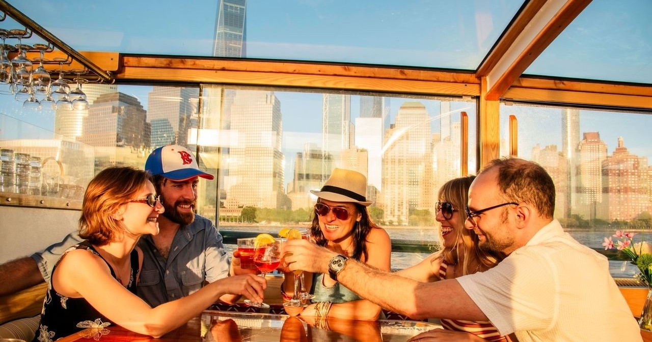 Five people toasting drinks on a boat with city skyline in background.