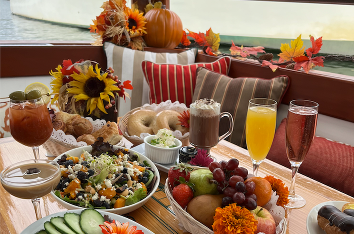 Autumn-themed brunch table with drinks, salad, fruit, bagels, and fall decorations.
