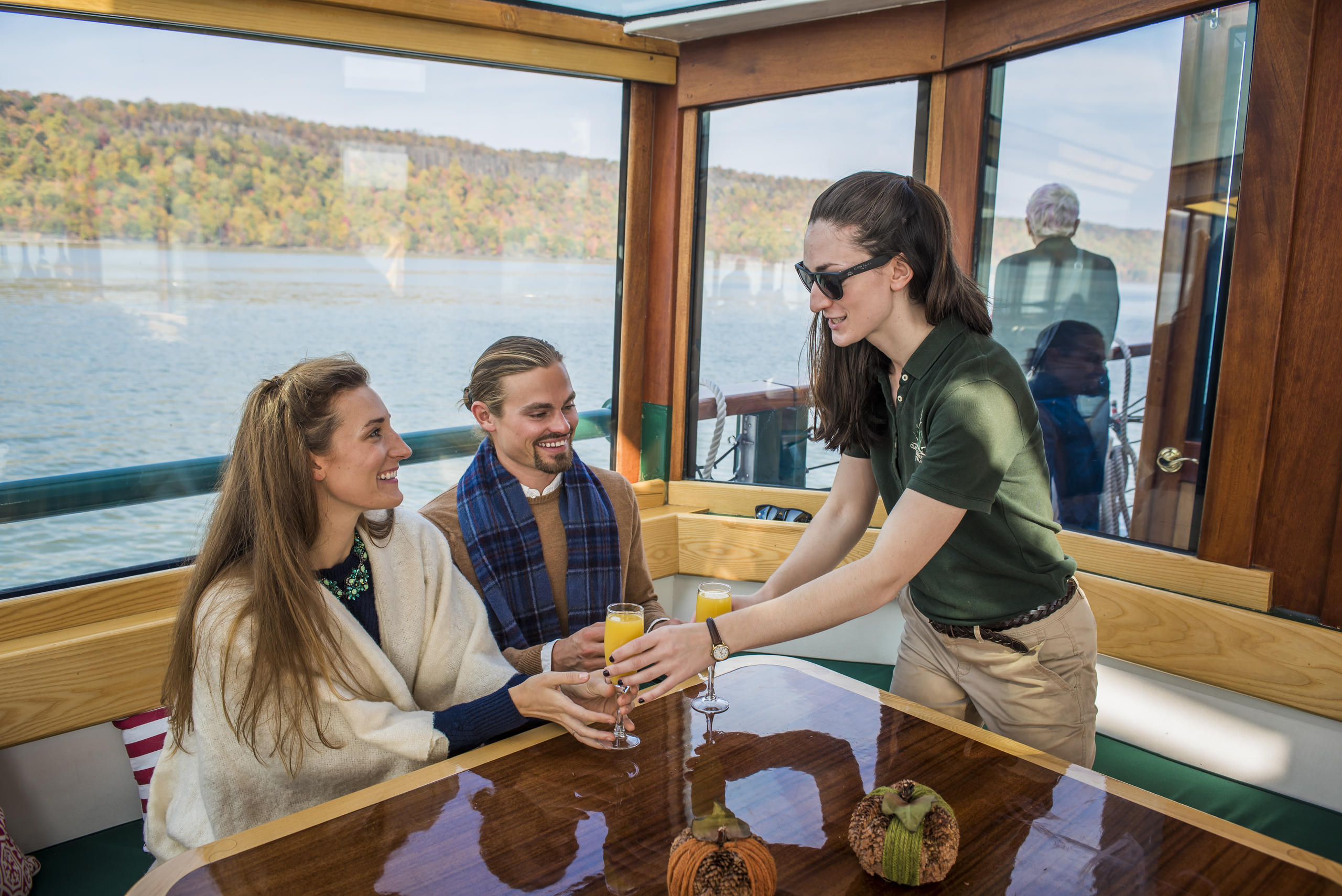 Two people being served drinks on a boat with a scenic lake view.
