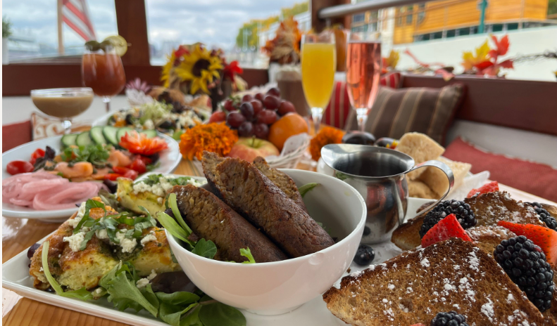 Close-up of a brunch spread with meats, fruits, and drinks on a table.