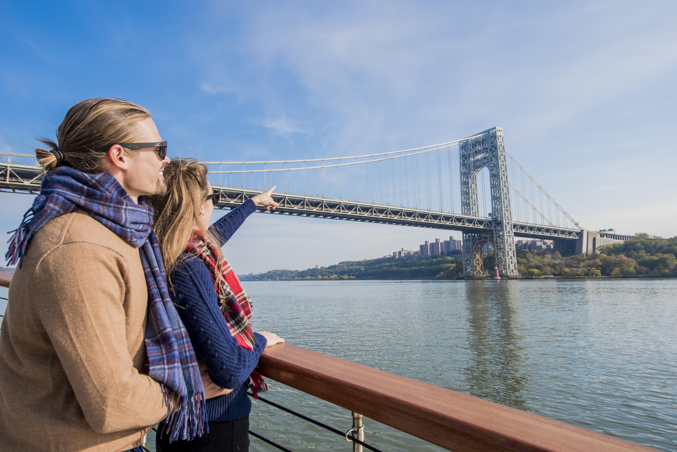 Two people on a boat admire a large suspension bridge over water.
