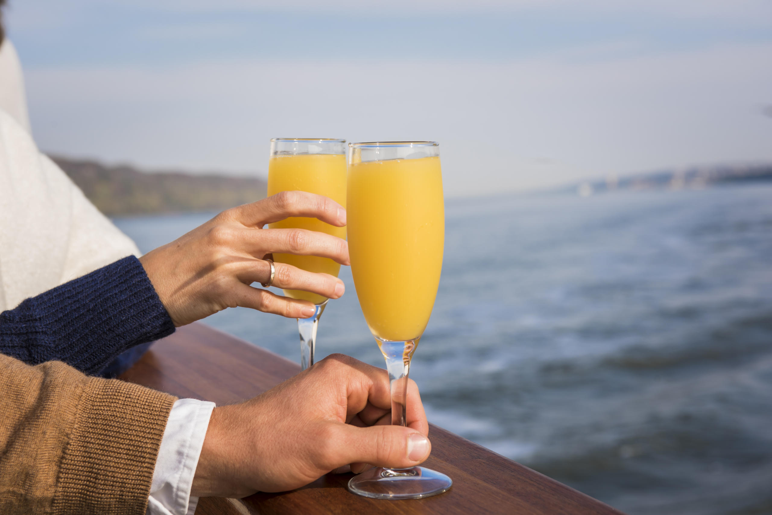 Two people clinking glasses of orange juice on a boat.