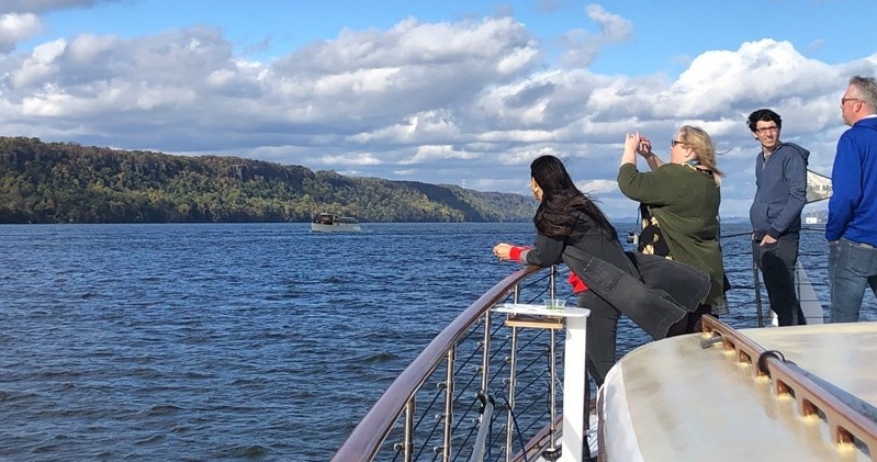 People on a boat enjoying a scenic view of a river and hills.