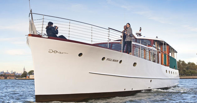 Large white yacht on water with two people posing for a photo.