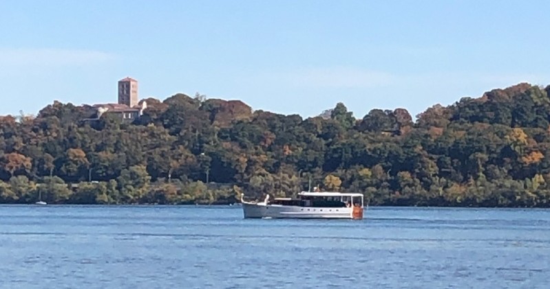 Boat on river with forested hill and tower in background.