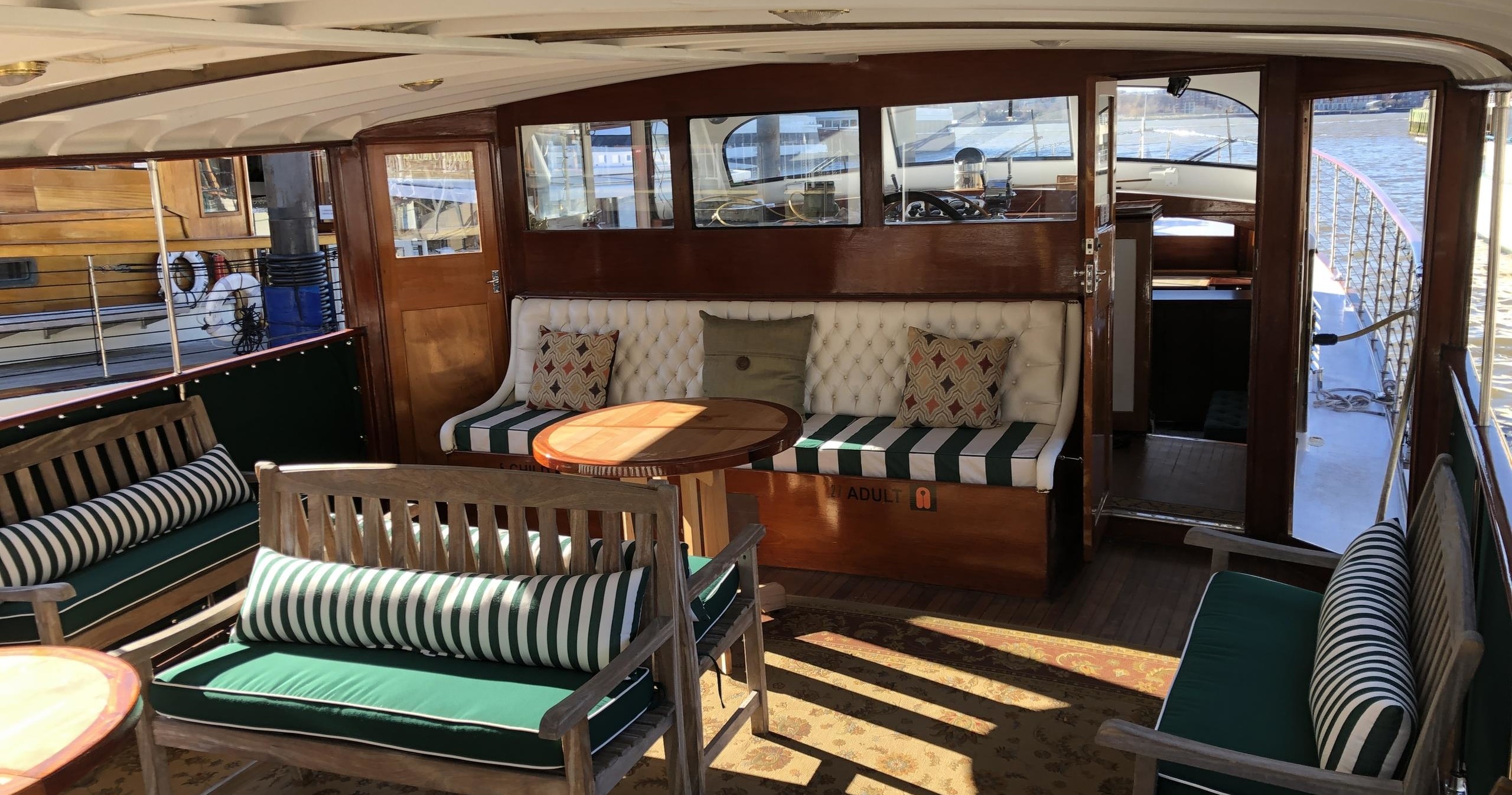 Interior of a boat with wooden furniture, striped cushions, and large windows.