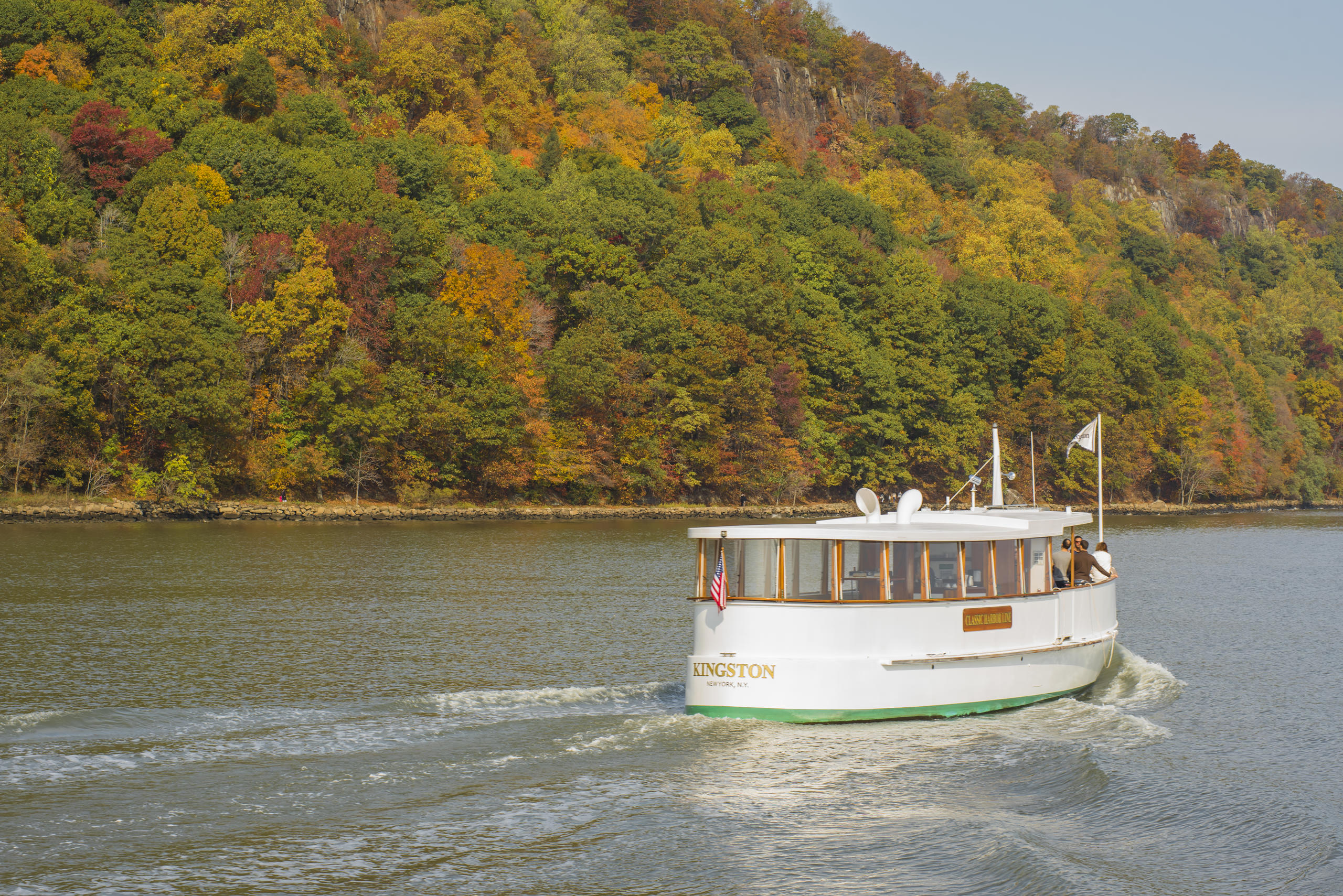 Boat on river with autumn trees on the bank in the background.