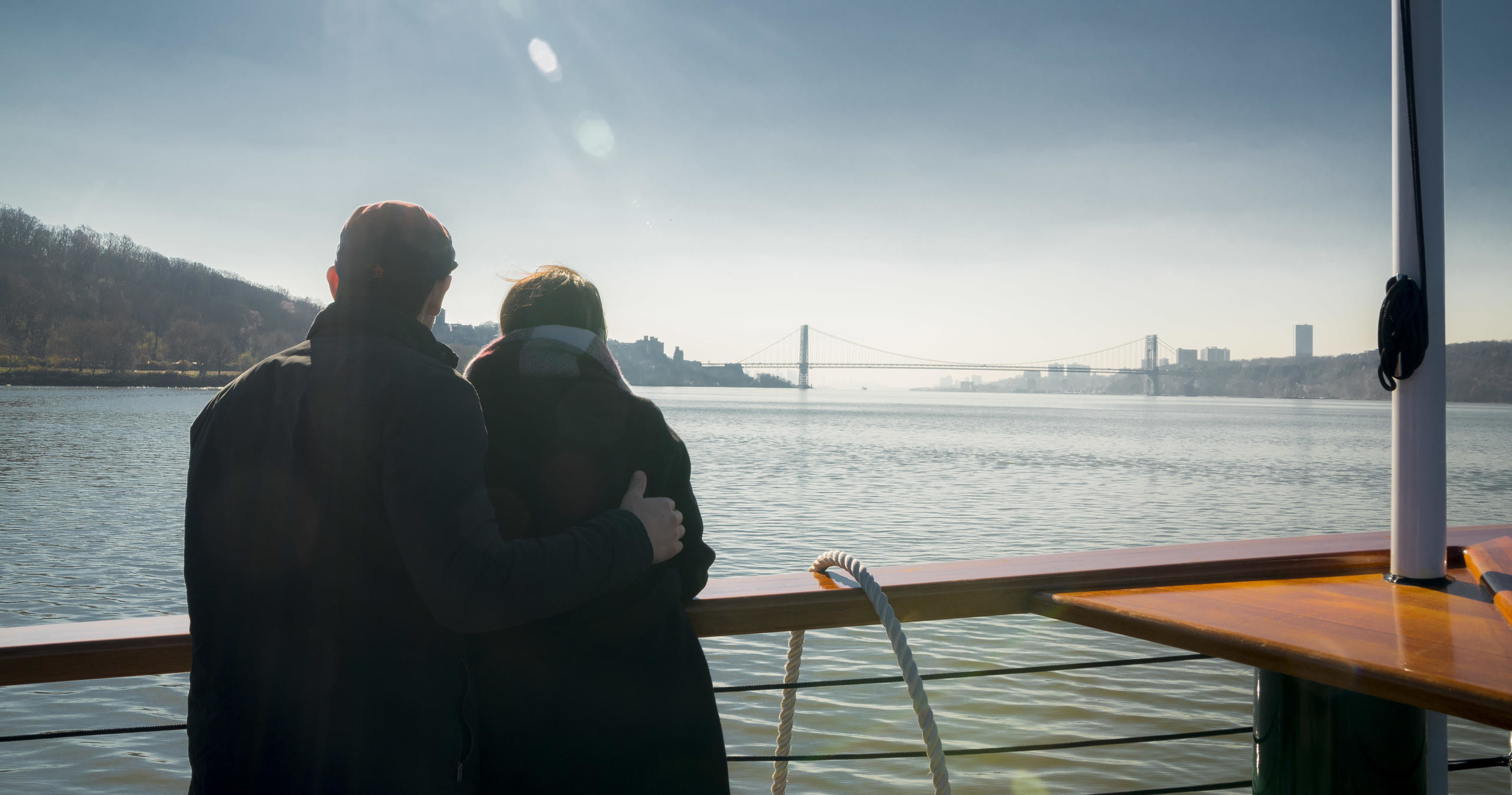 Two people on a boat, gazing at a distant bridge over the water.