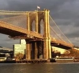 Brooklyn Bridge with a boat passing underneath at sunset.