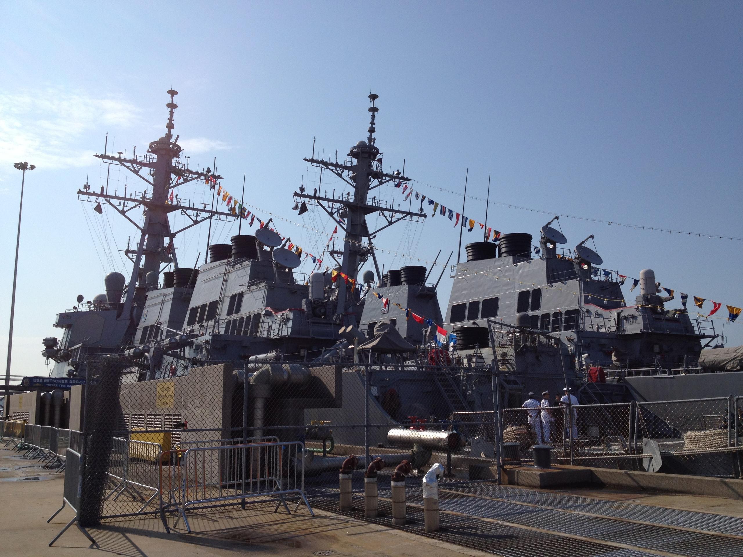 Two navy warships docked with flags and crew on deck.