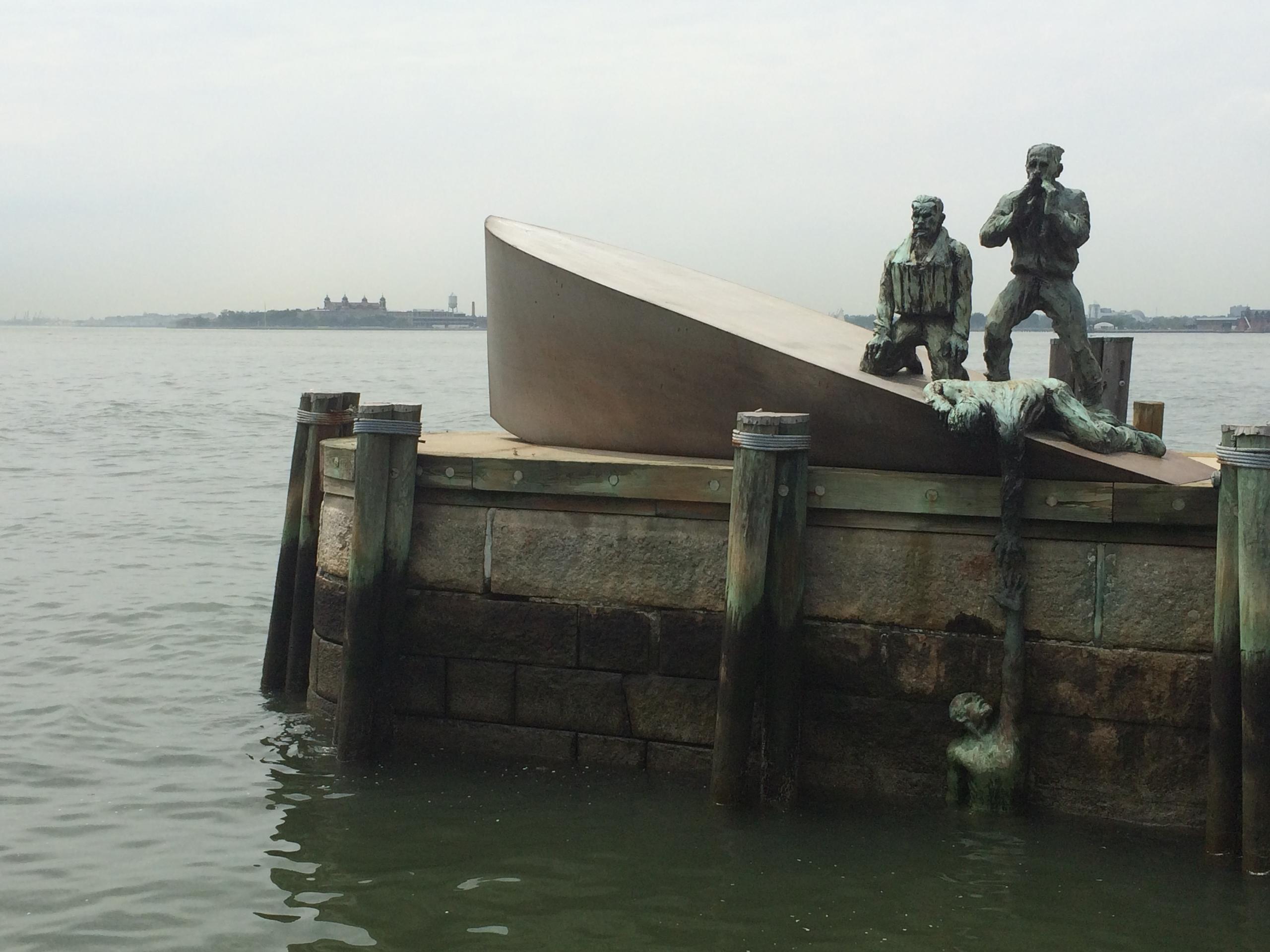 Bronze sculpture of sailors rescuing a man on waterside platform.