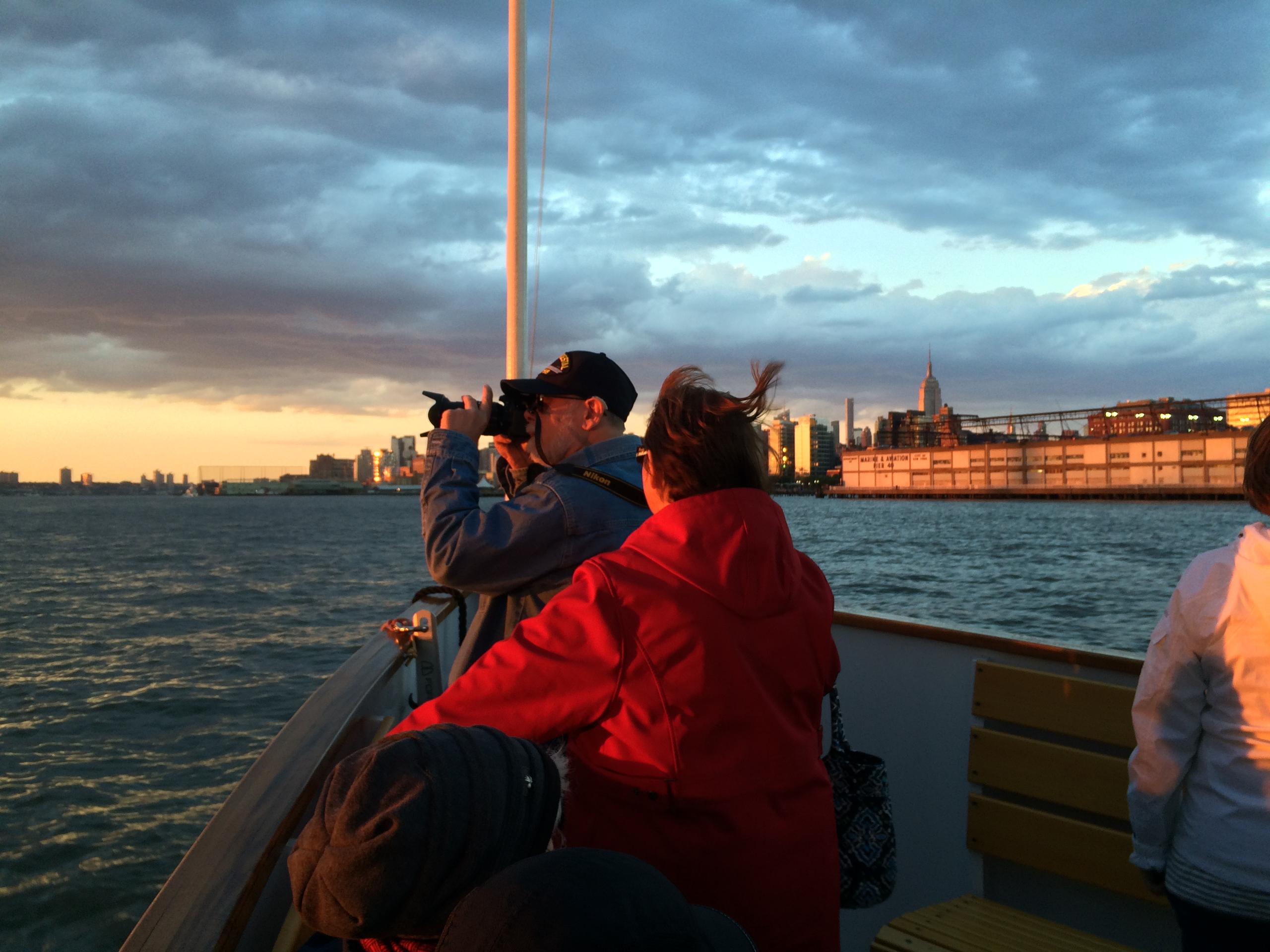 People on a boat photographing a cityscape at sunset.