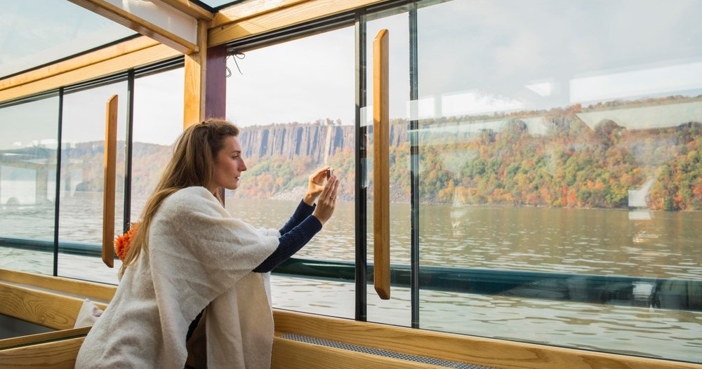 Woman looking out a window at a river and autumn trees.