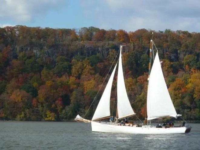White sailboat on a lake with autumn trees in the background.