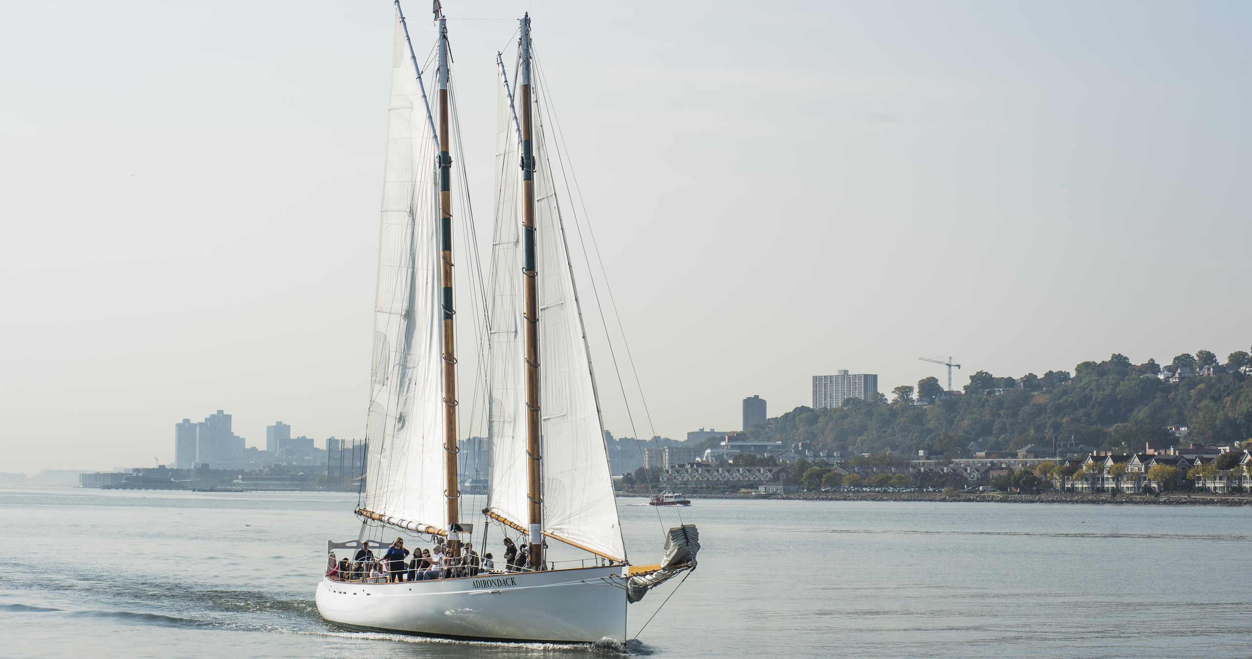 A sailboat with two masts on a calm sea near a shoreline with buildings.