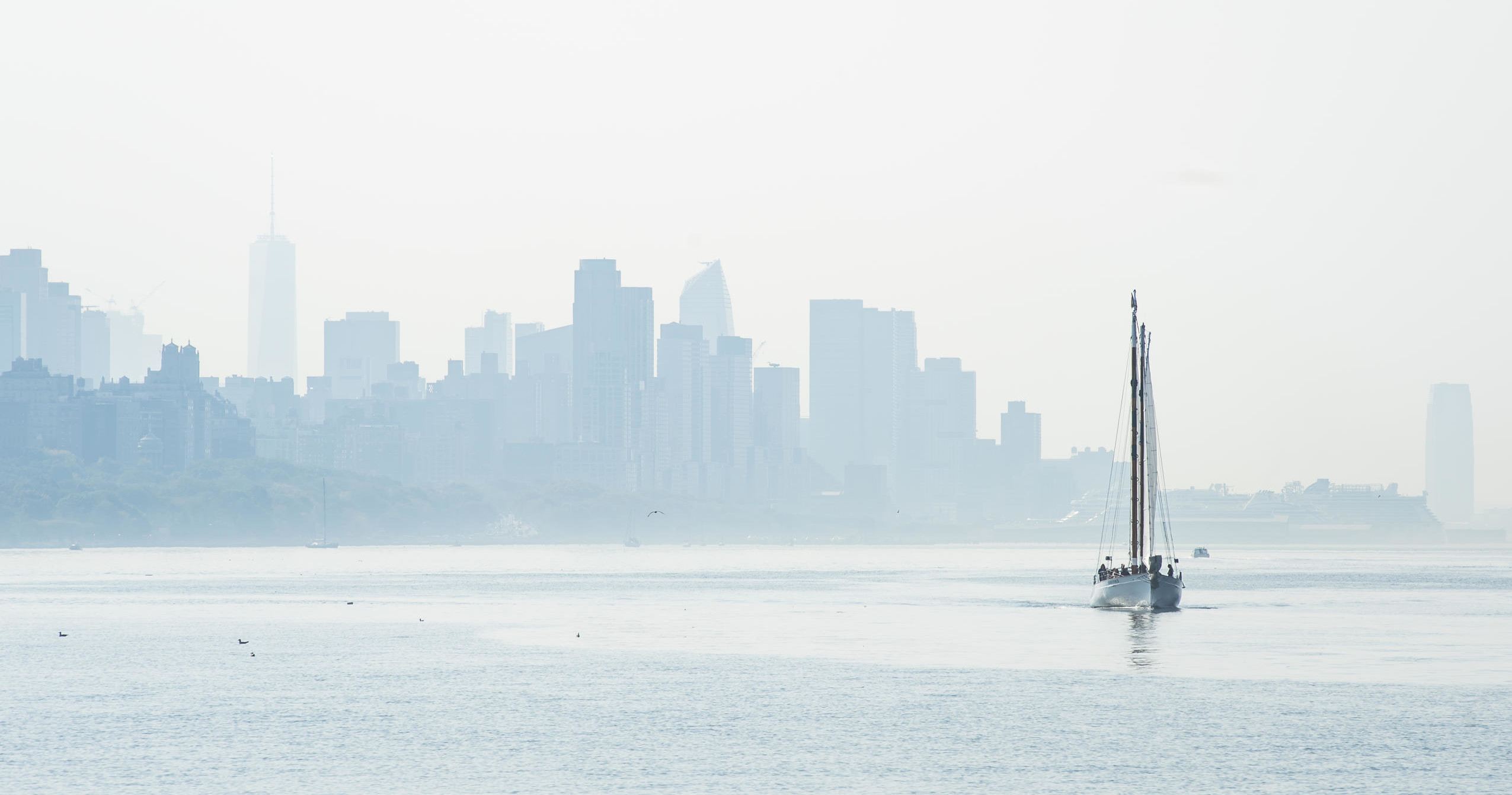 Sailboat on misty water with city skyline in background.