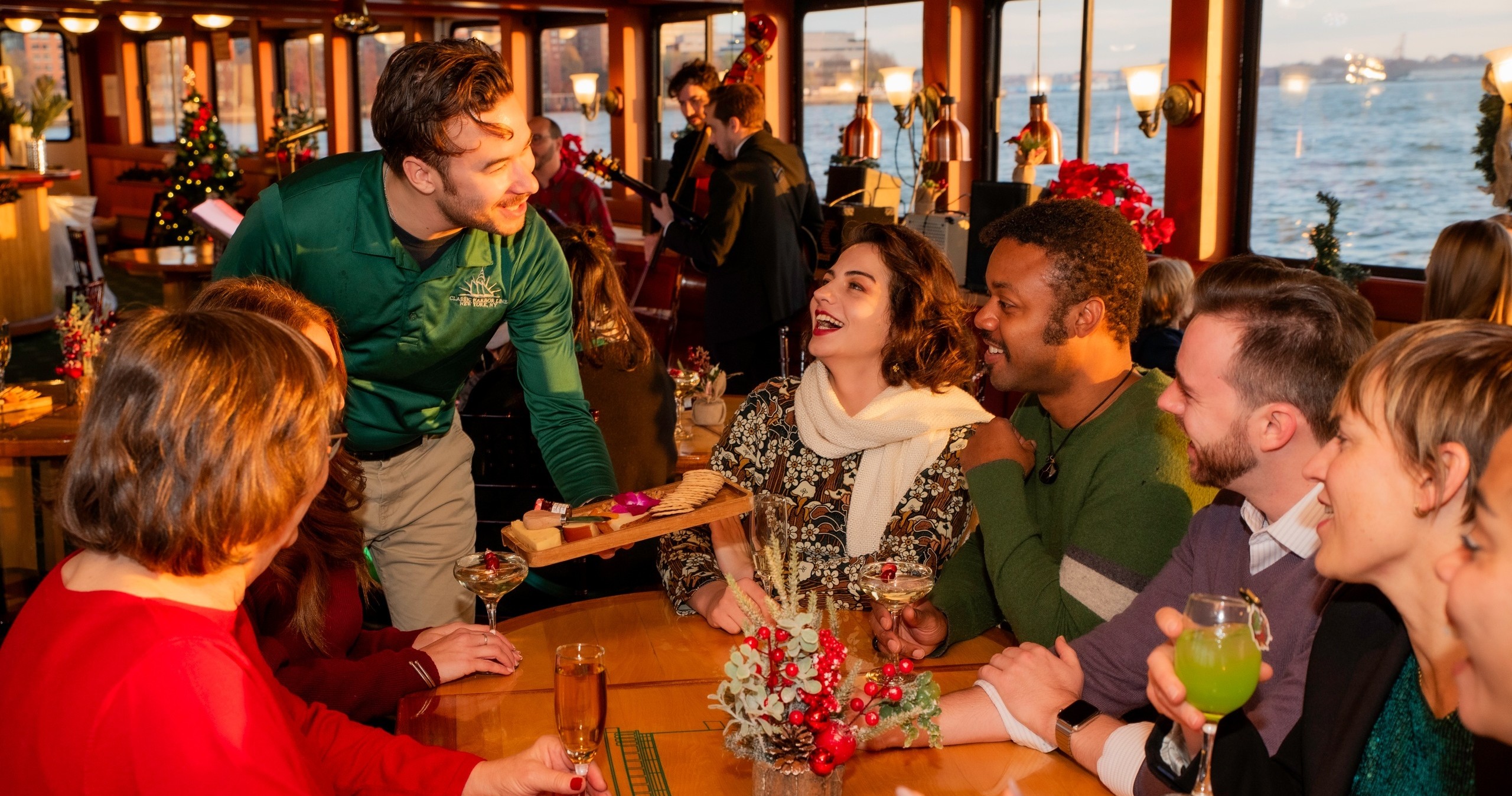 Group of people on a festive boat enjoying drinks, served by a waiter.