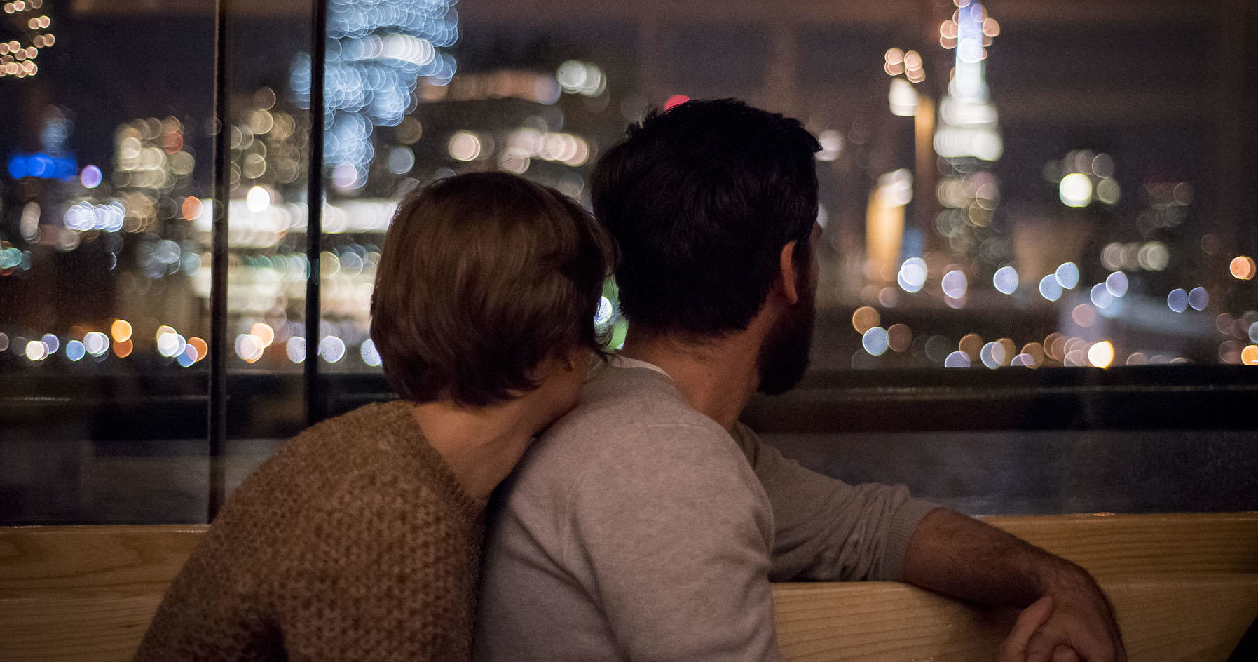 Couple gazes at city skyline through window at night.