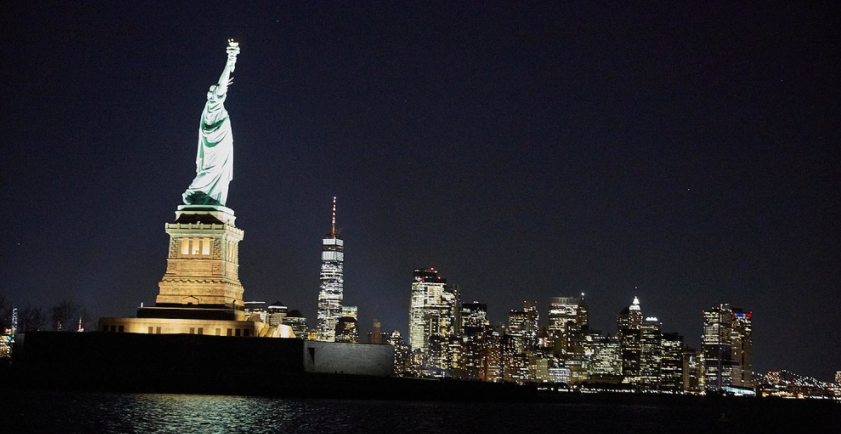 Statue of Liberty at night with New York City skyline in background.