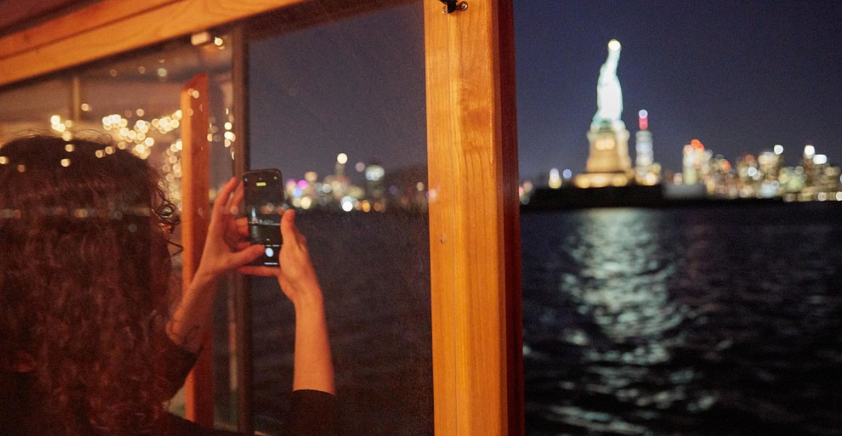 Person taking photo of Statue of Liberty at night from boat window.