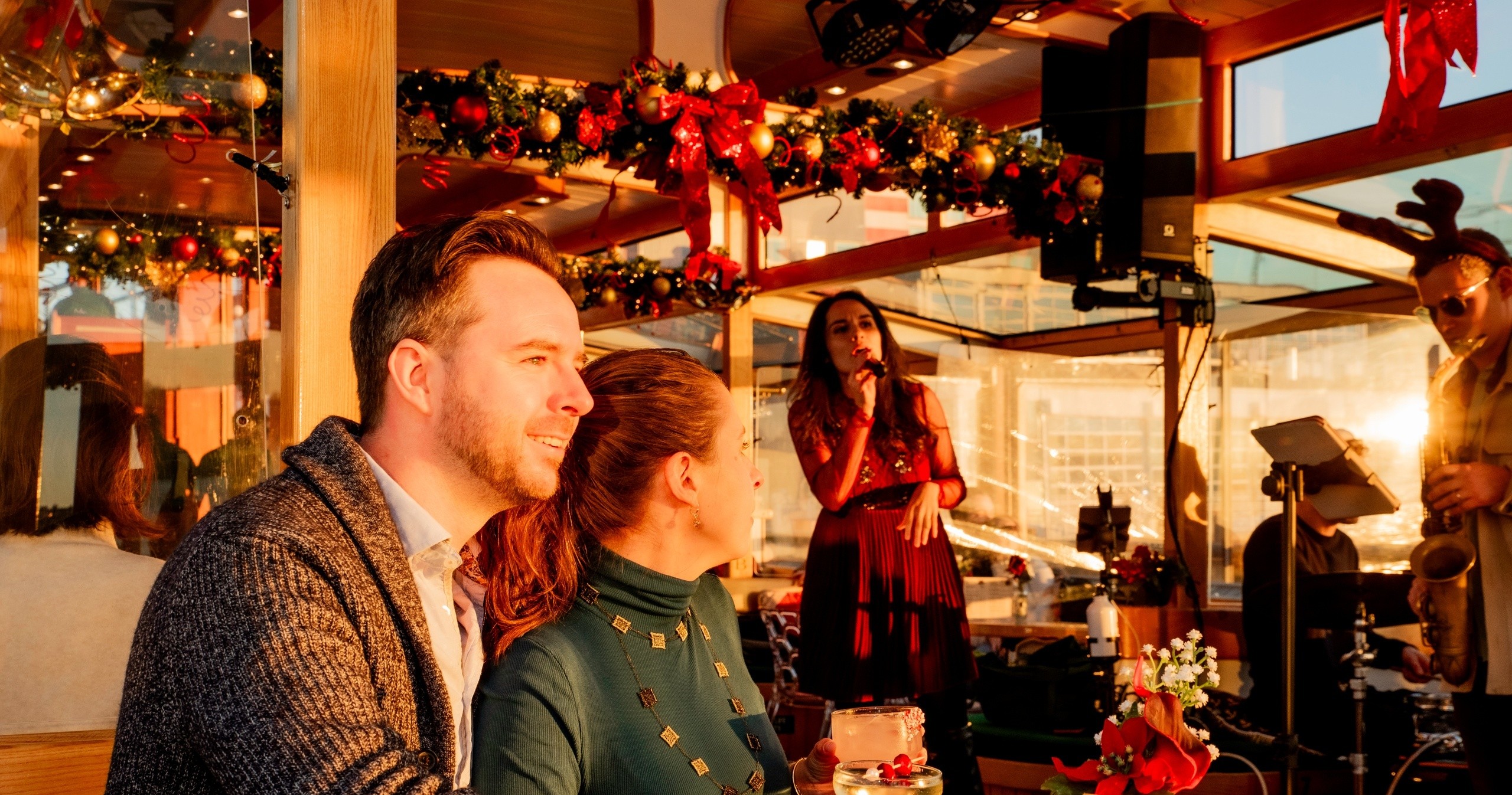 Couple in holiday decor cafe watching a woman sing into a microphone.