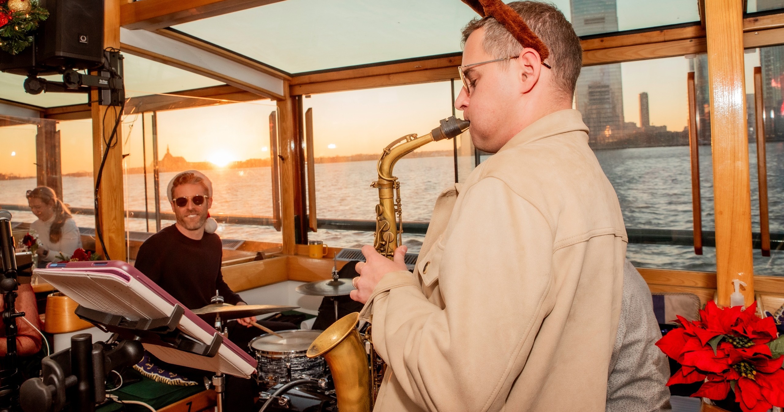 Musician playing saxophone on a boat at sunset with city skyline.