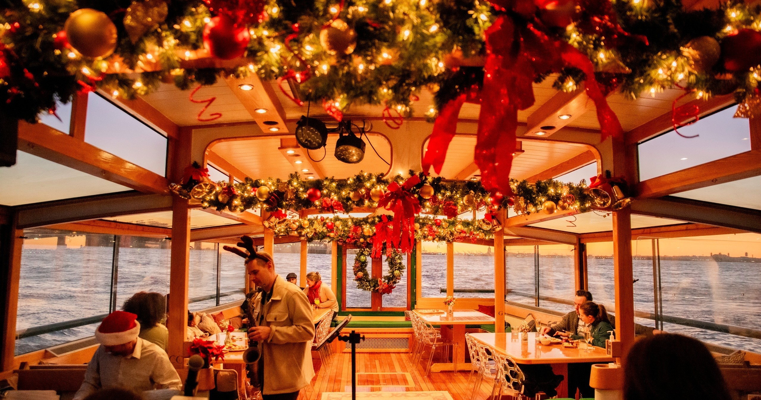 Festive boat interior with garlands and lights, people dining.