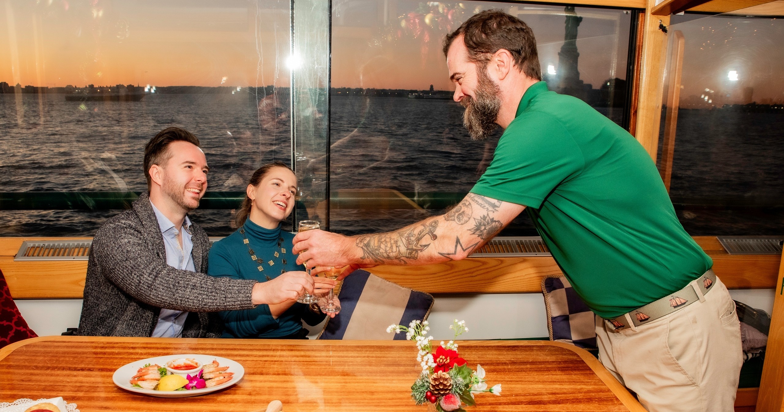 Couple on boat being served drinks by man with beard.