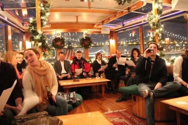 People singing on a decorated boat at night, with festive lights and city view.