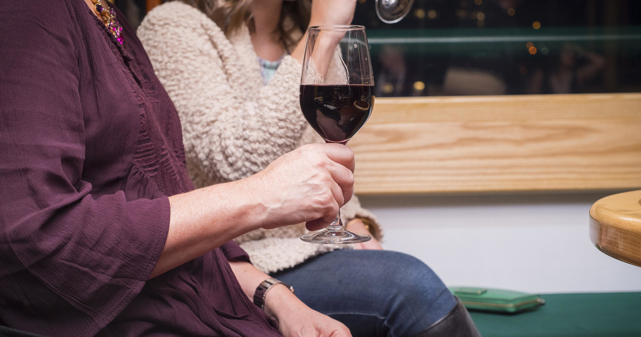 Two people seated, holding glasses of red wine indoors.