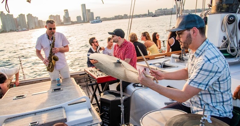 Musicians play on a boat with a city skyline in the background.