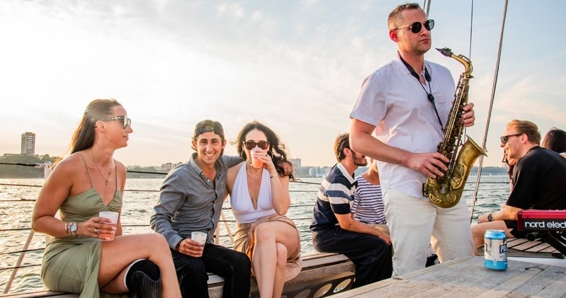 People on a boat enjoying drinks, with a saxophonist playing music.