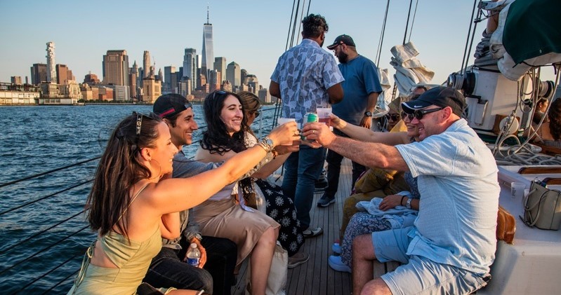 People toast on a boat with city skyline in background.