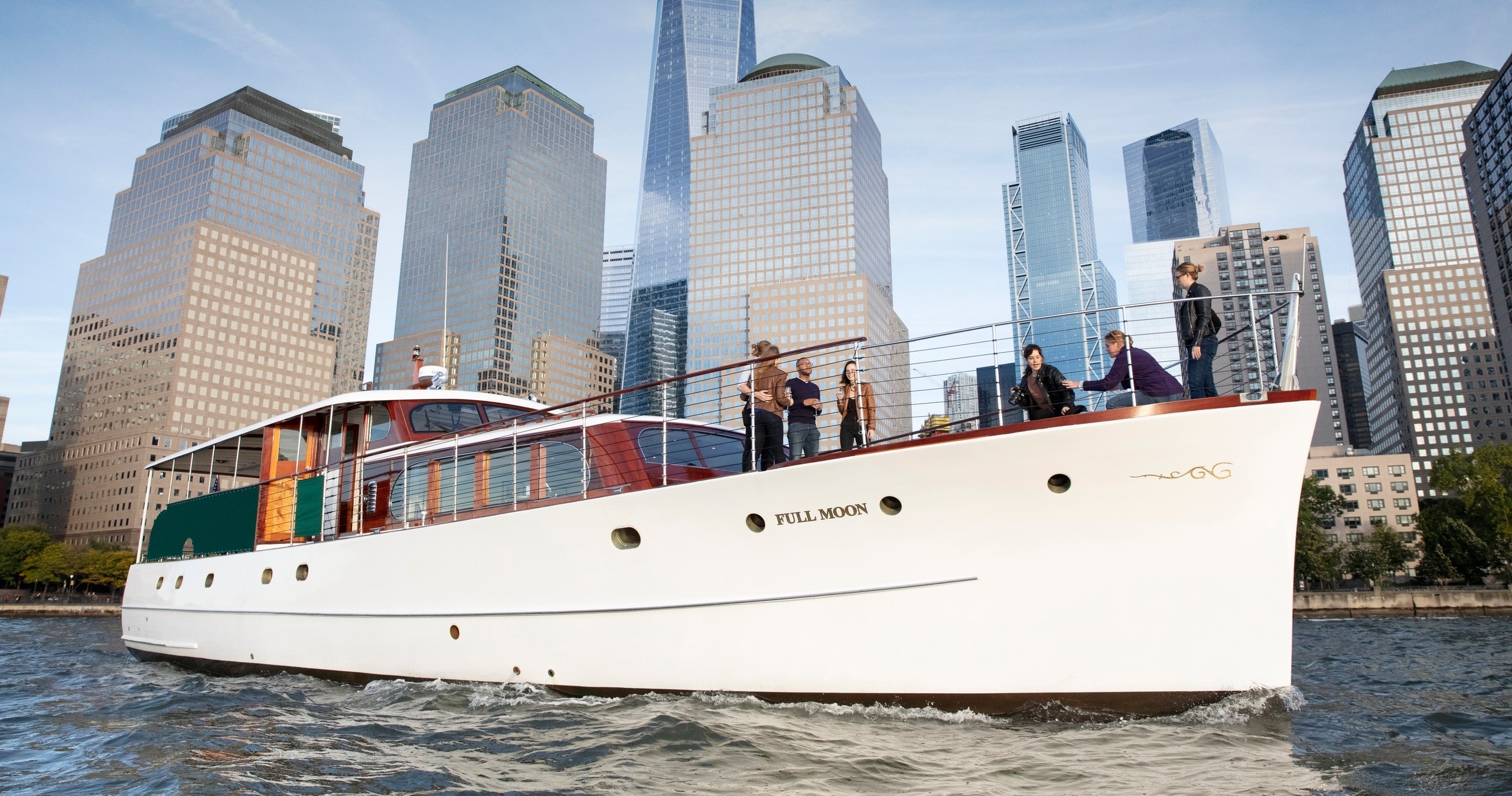 People on a white yacht in front of city skyscrapers.
