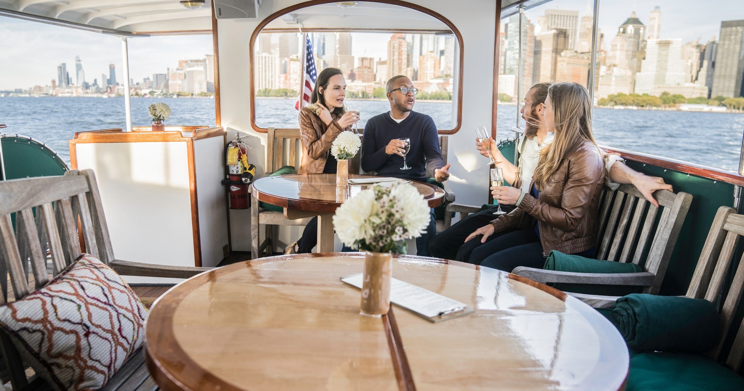 Group of people chatting on a boat with city skyline in background.