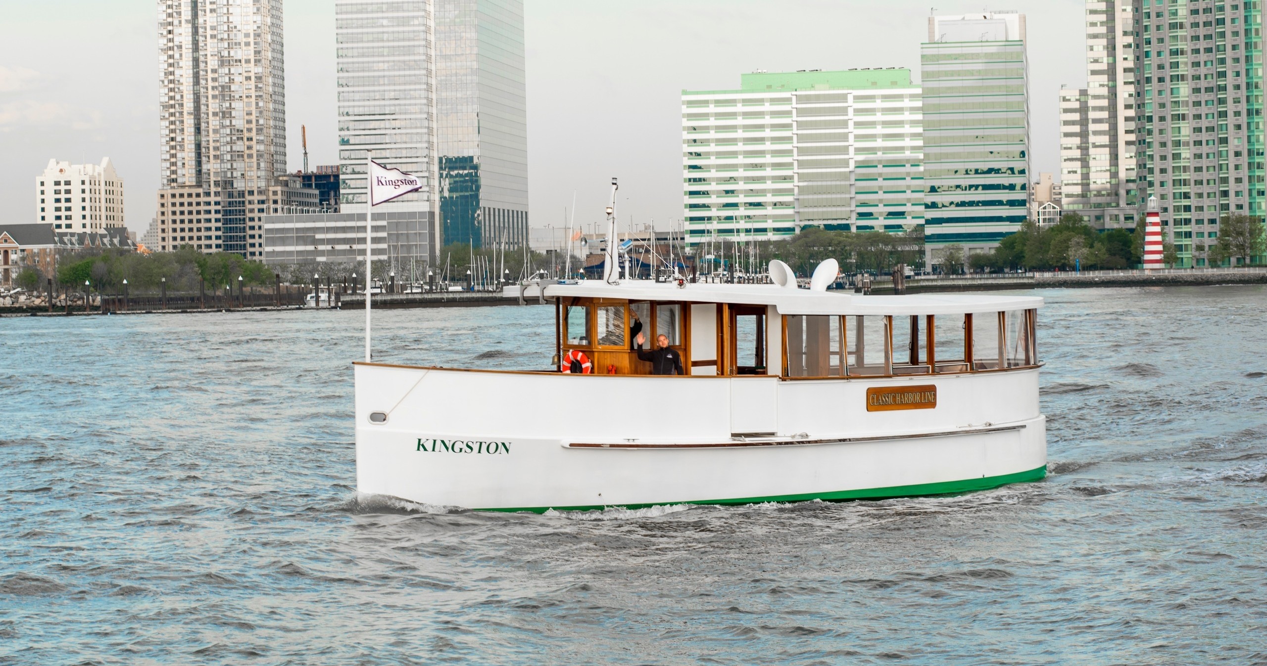 Small white boat on river with city buildings in background.