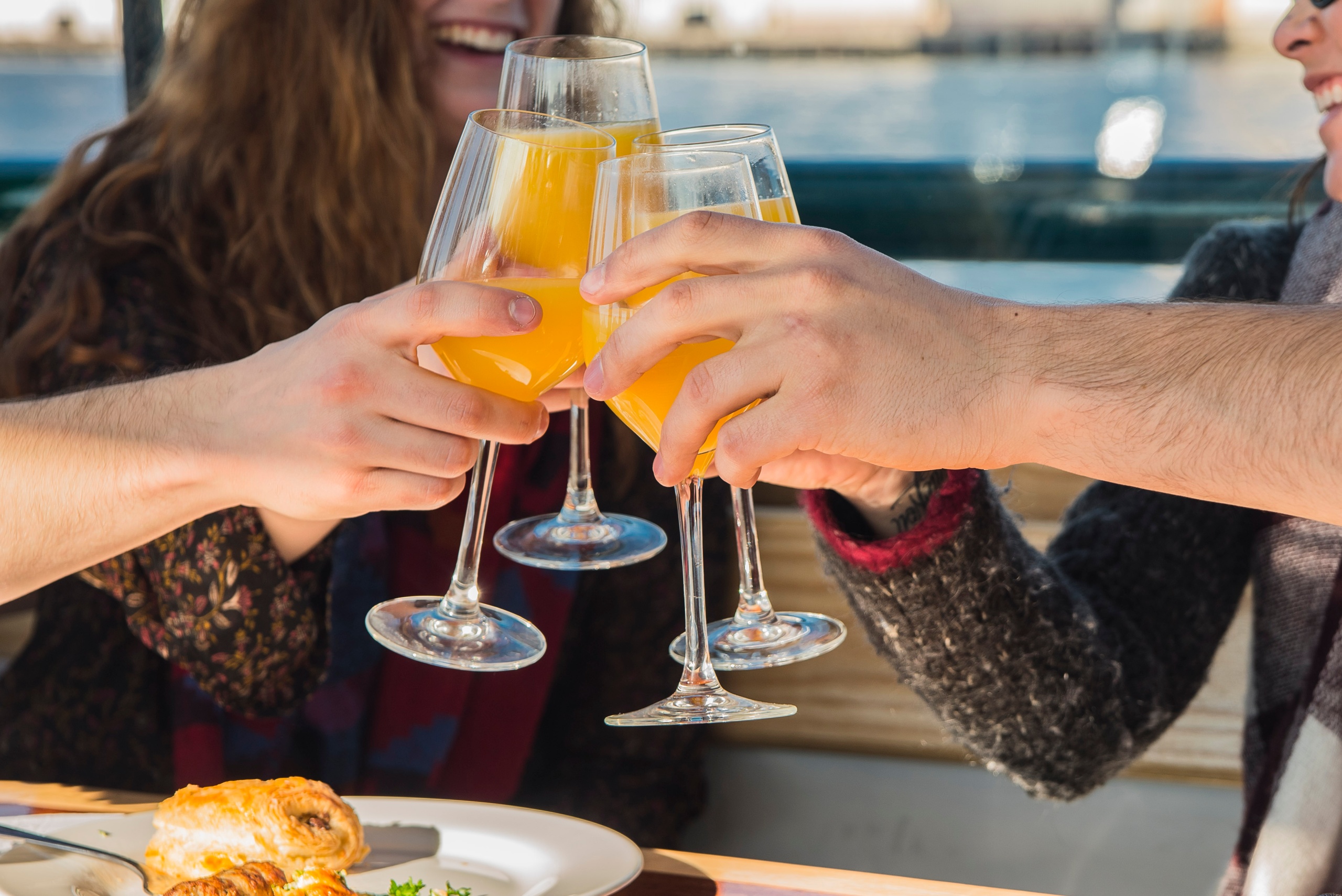 Four people clinking glasses of orange drinks at a table.