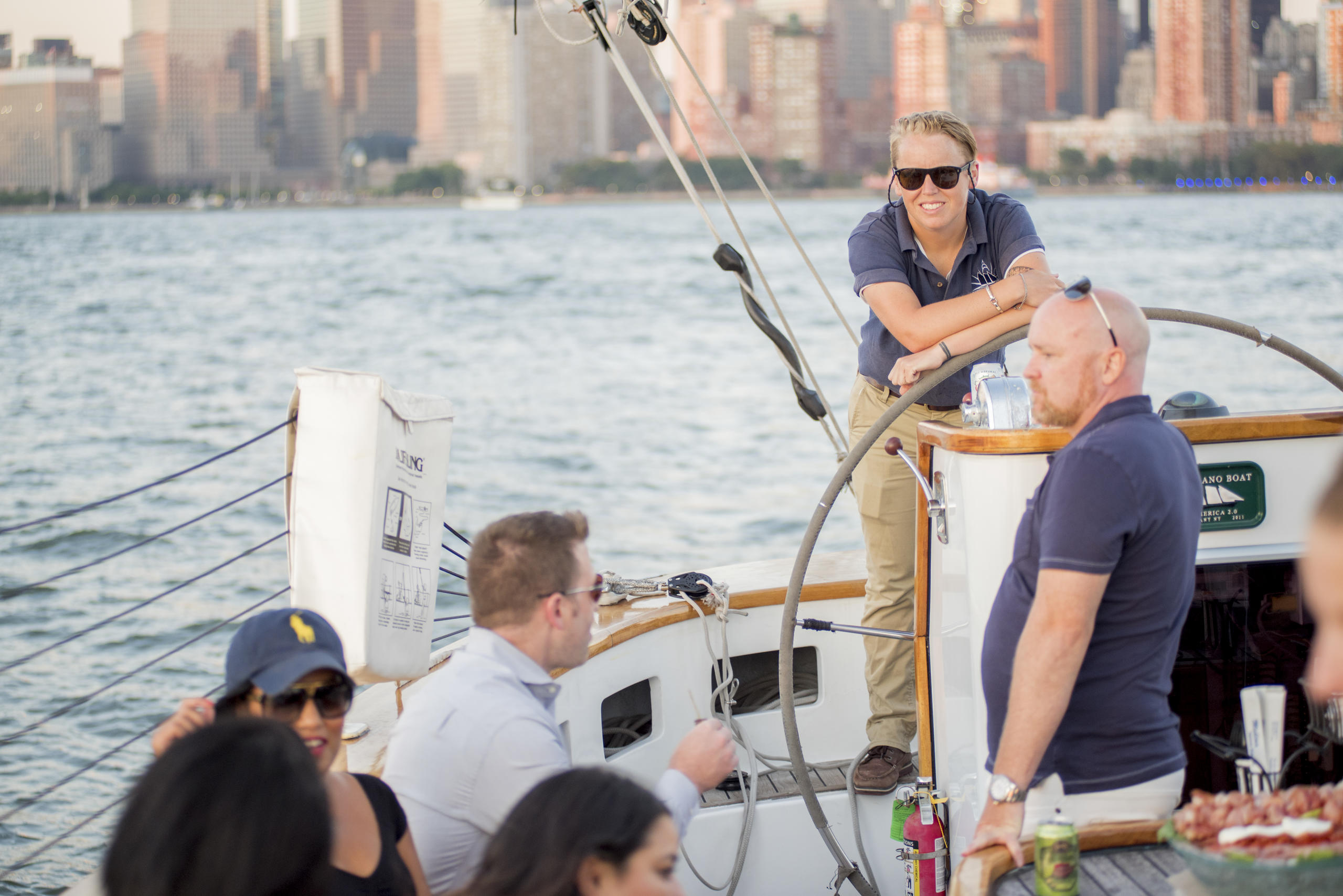 People relaxing on a sailboat with a city skyline in the background.