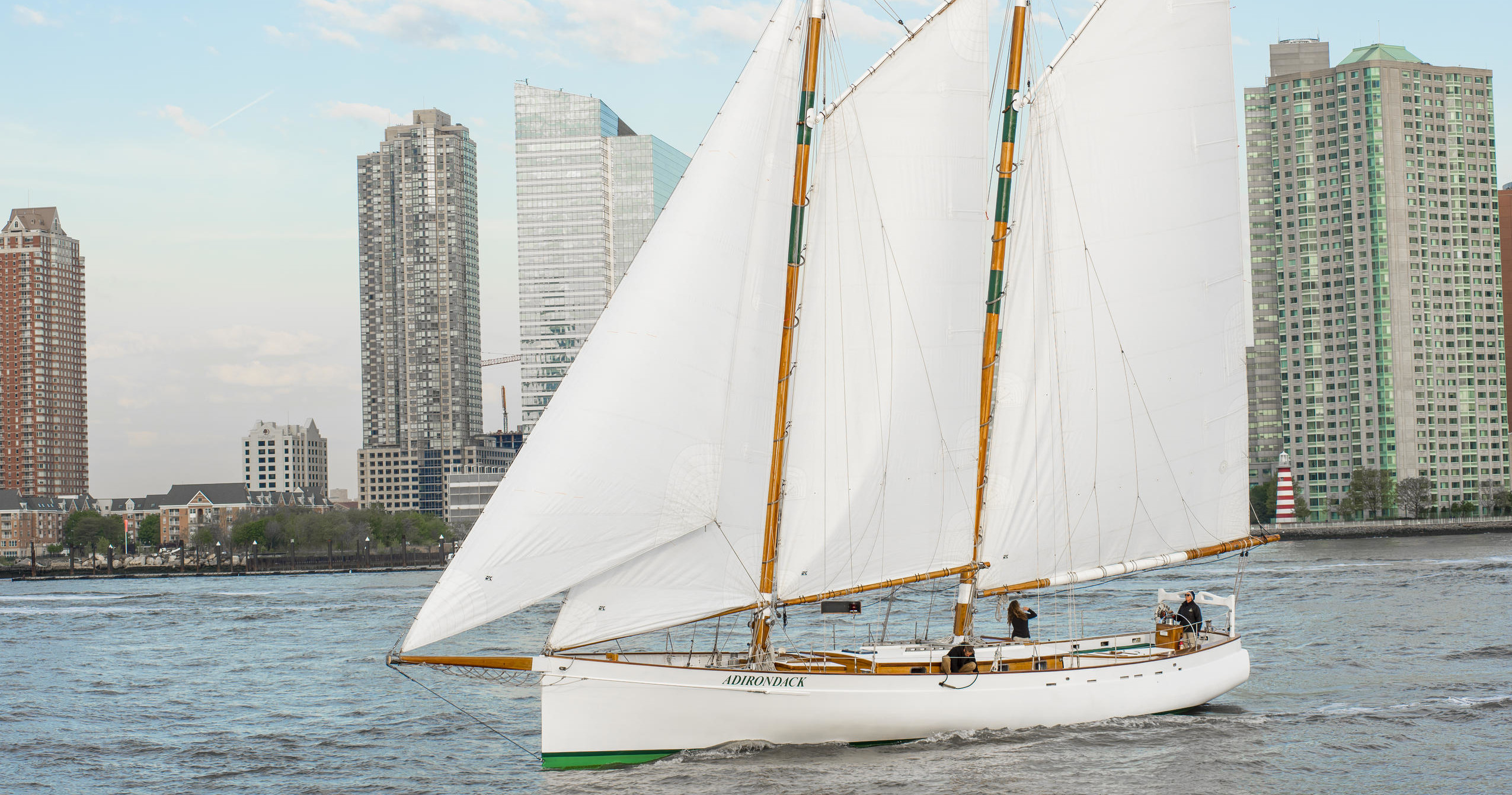 Sailboat on river with city skyscrapers in background.
