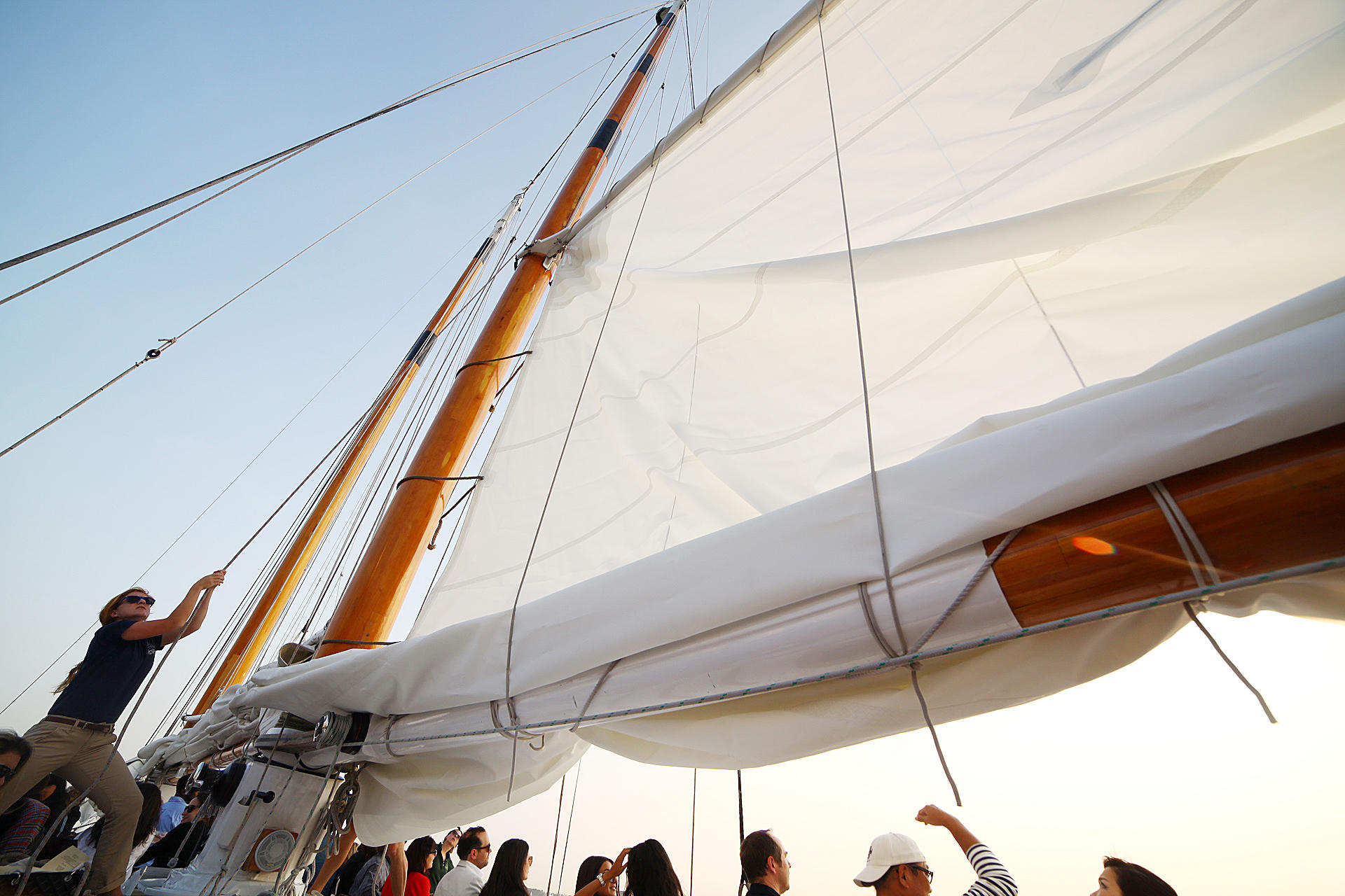 People on a sailboat adjusting large white sails with wooden masts.