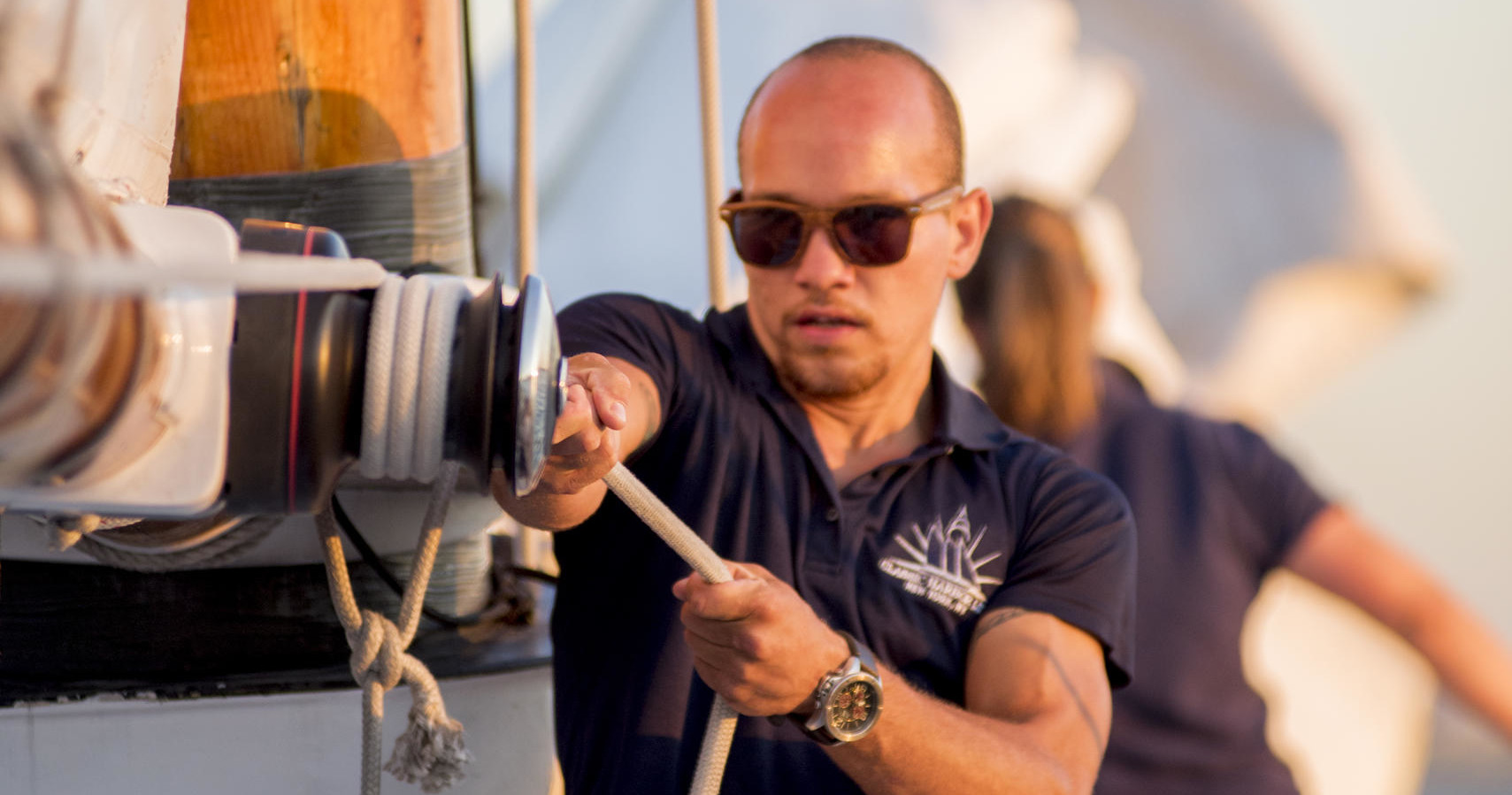 Man in sunglasses adjusting sail ropes on a boat.