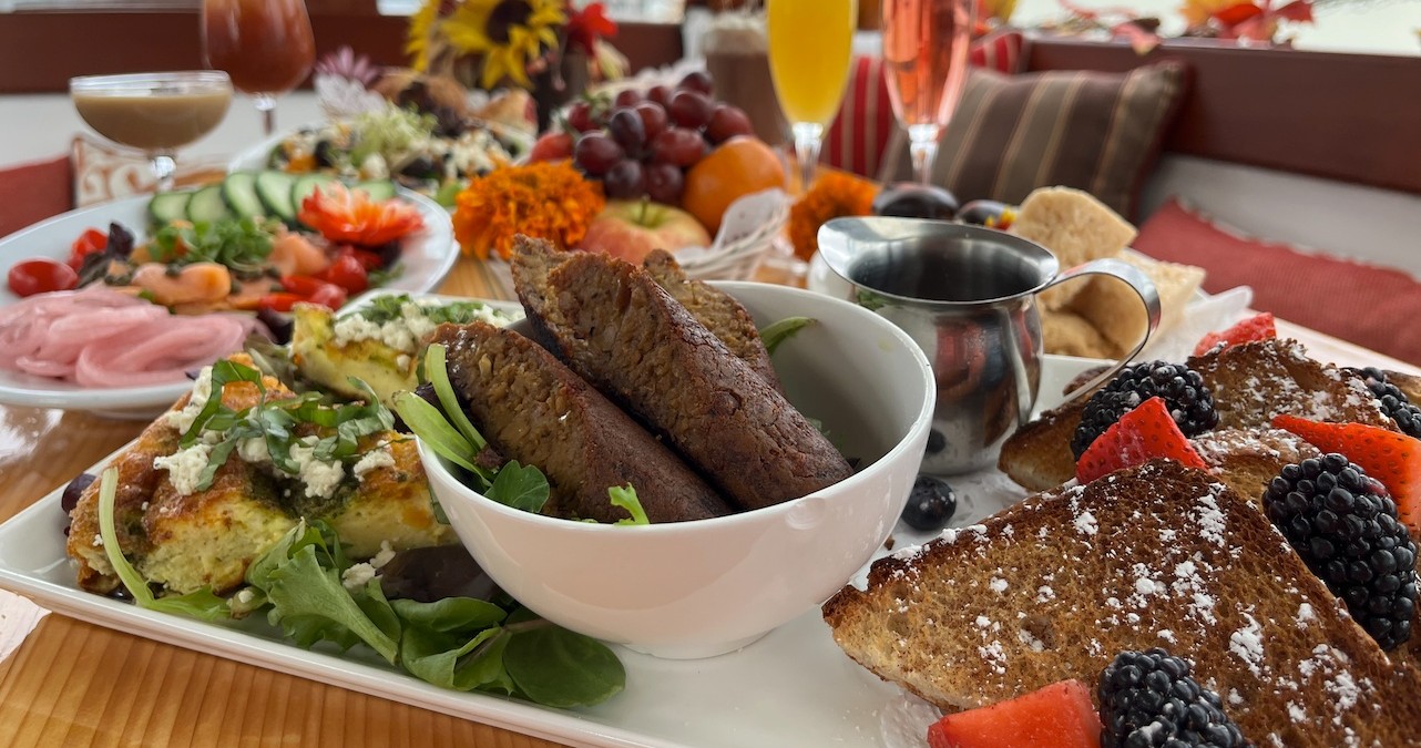 Assorted brunch foods including toast, sausages, and fruit, with drinks in a cozy setting.