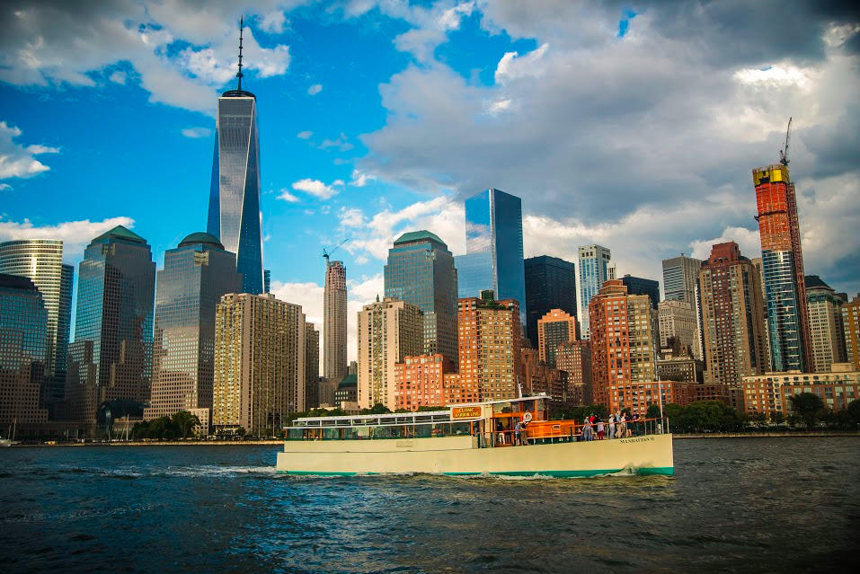 Boat on river with a city skyline and tall buildings in the background.