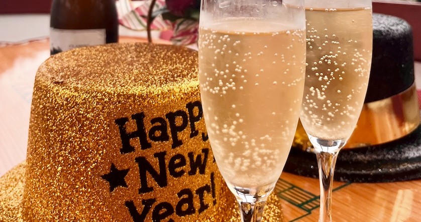 Two champagne flutes and a glittery gold New Year's hat on a table.