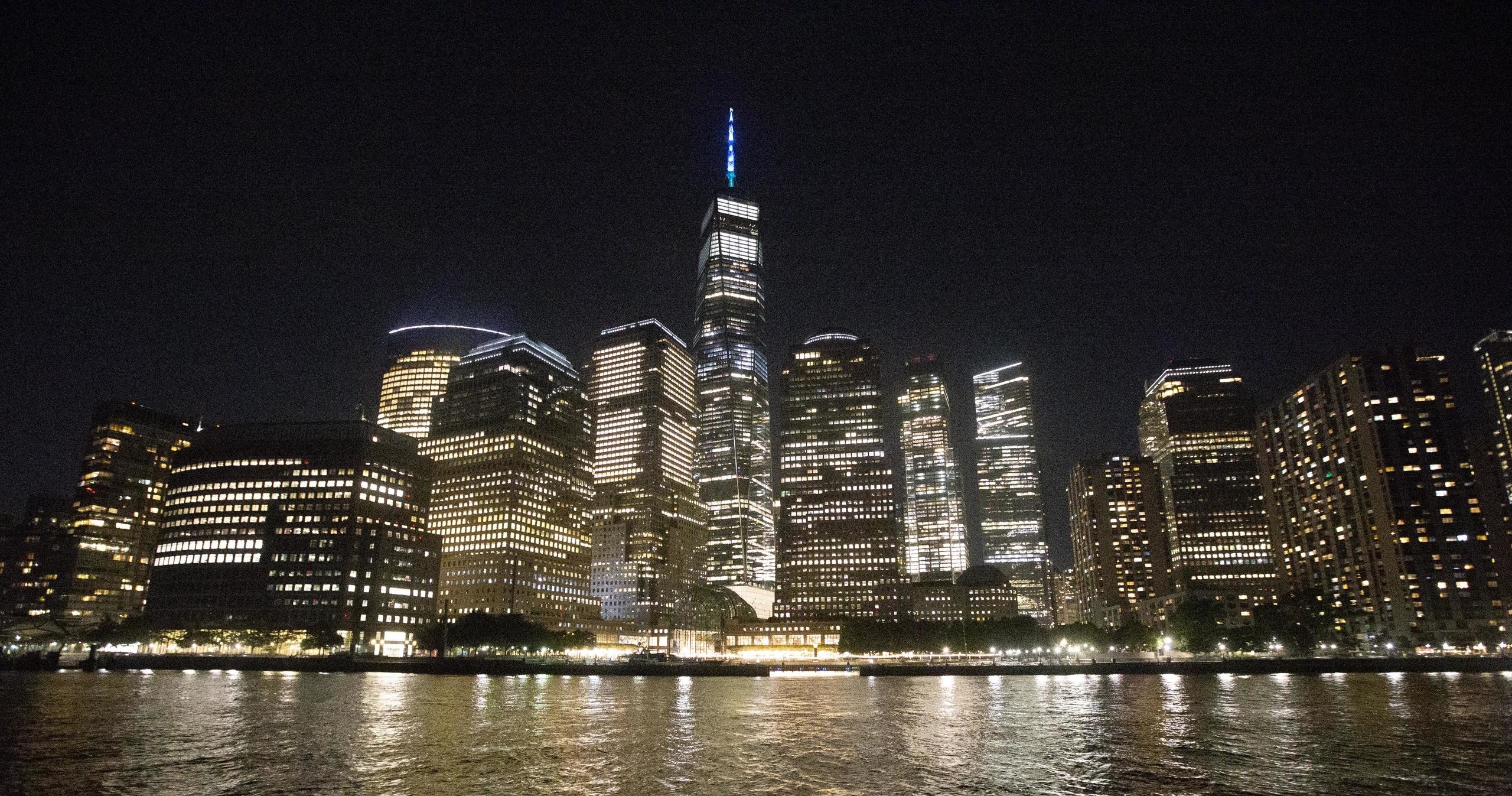 City skyline at night with illuminated skyscrapers reflected in water.