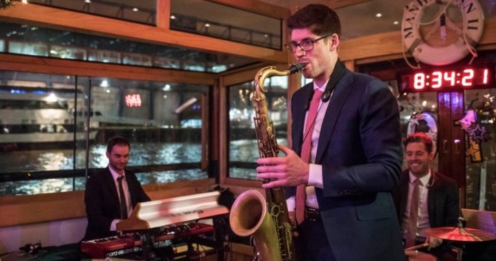 Musicians in suits playing saxophone and keyboards in a room with large windows.