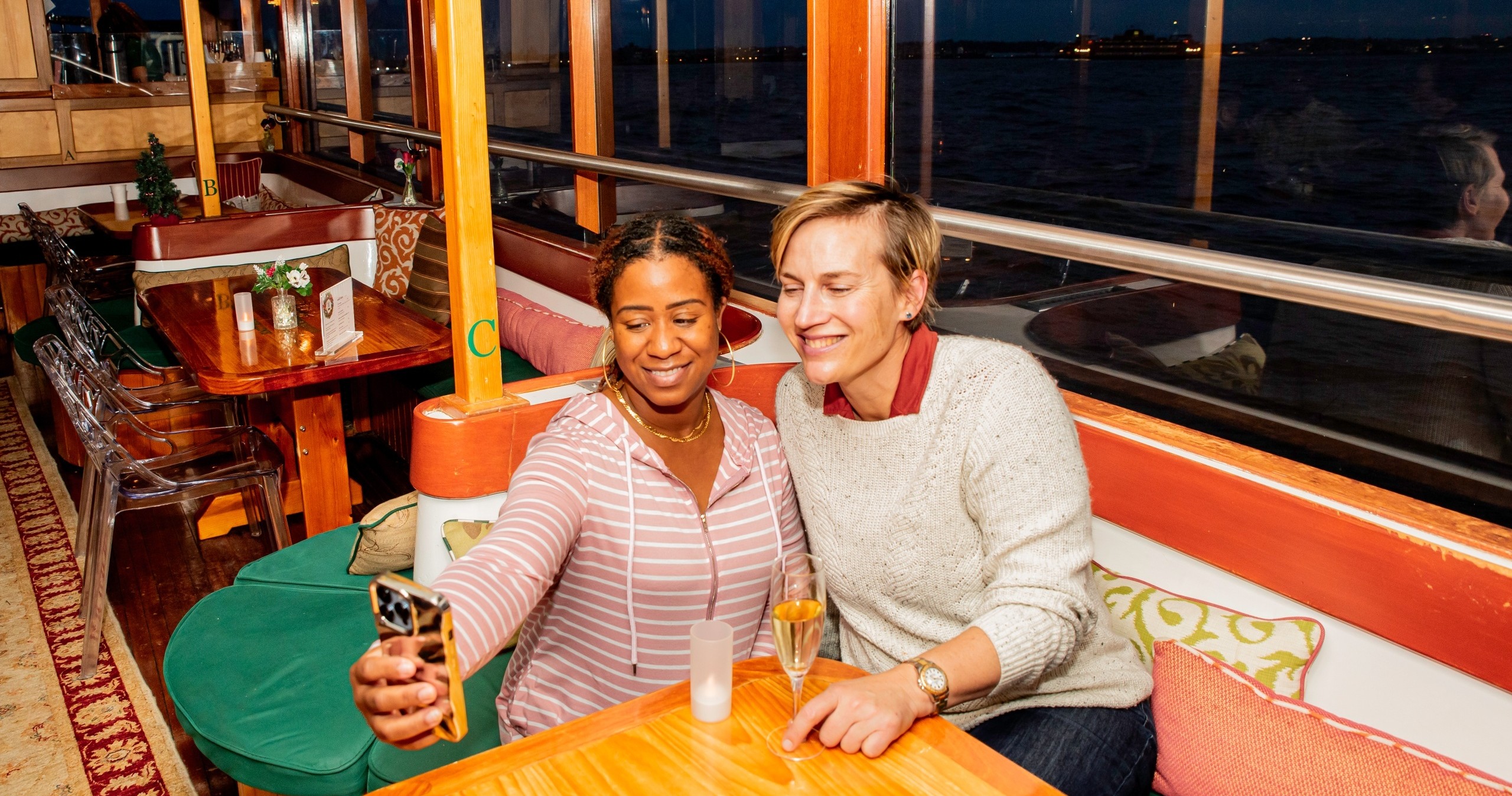 Two people on a boat sitting at a table, taking a selfie, with drinks.